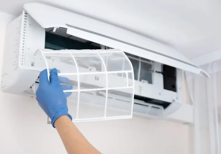 A hand wearing latex gloves holding an air conditioning filter during the process of maintenance