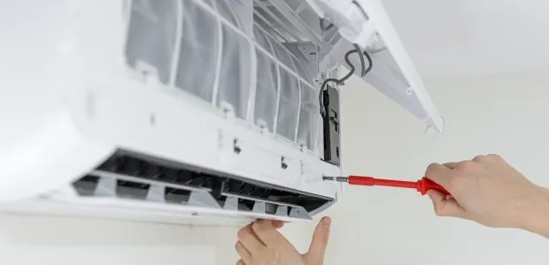 A hand with tool used to repair the air conditioning unit on the wall of a house