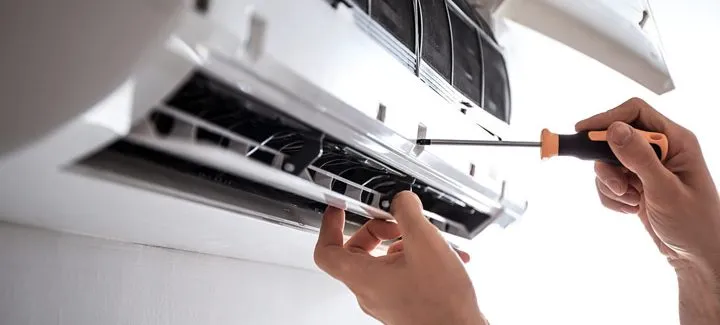 A hand with screwdriver securing the screw lock of the air conditioning unit cover