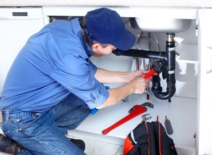 A professional plumber working on the under sink pipes with his handy tools